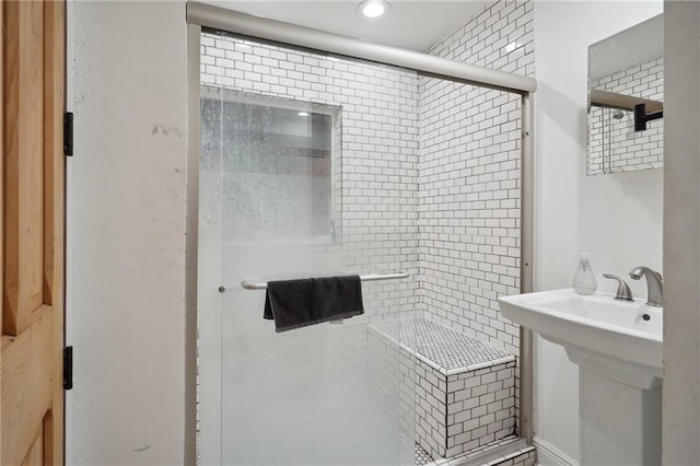 bathroom featuring a shower with shower door and sink