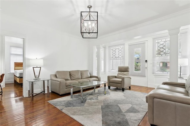 living room with a notable chandelier, ornate columns, dark wood-type flooring, and ornamental molding