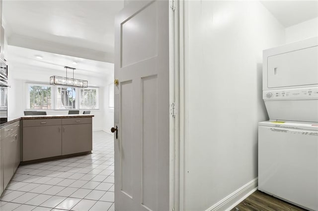 laundry area with a chandelier, stacked washer and clothes dryer, and light tile patterned flooring