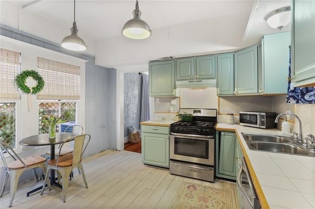 kitchen featuring sink, light wood-type flooring, stainless steel appliances, and hanging light fixtures