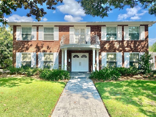 view of front of home with brick siding, a balcony, and a front lawn