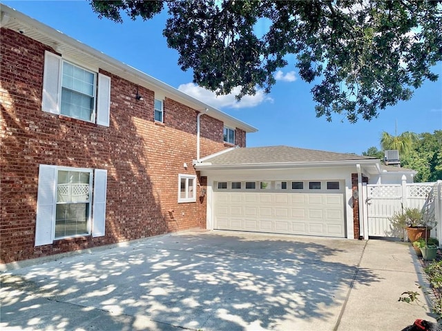 view of side of home featuring driveway, a gate, fence, a garage, and brick siding