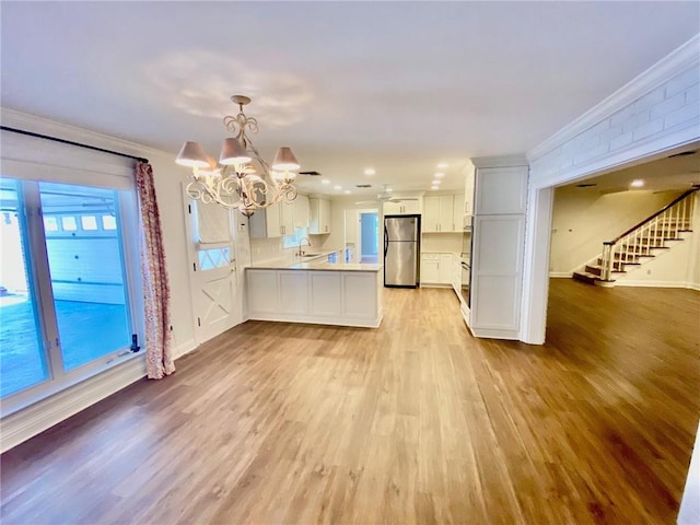 kitchen featuring ornamental molding, freestanding refrigerator, a peninsula, light wood finished floors, and light countertops