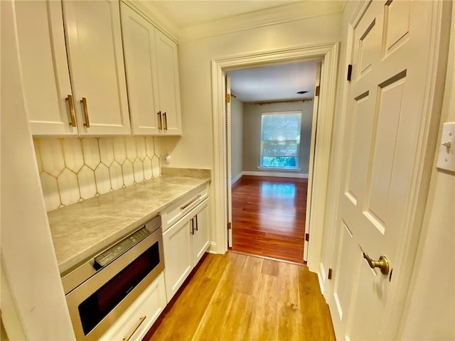 bar featuring stainless steel microwave, baseboards, crown molding, and light wood finished floors