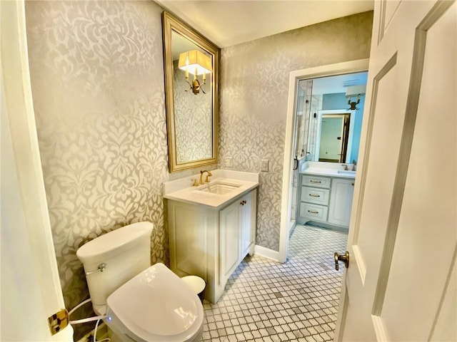 bathroom with baseboards, toilet, vanity, and wallpapered walls