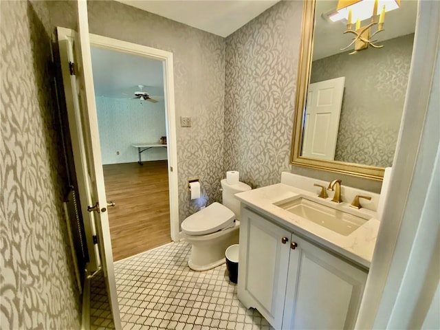 bathroom featuring tile patterned floors, toilet, wallpapered walls, ceiling fan, and vanity