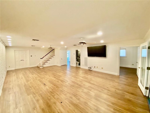 unfurnished living room with stairs, a ceiling fan, baseboards, and light wood finished floors