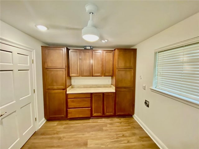 kitchen featuring baseboards, decorative light fixtures, light countertops, light wood-style flooring, and brown cabinetry