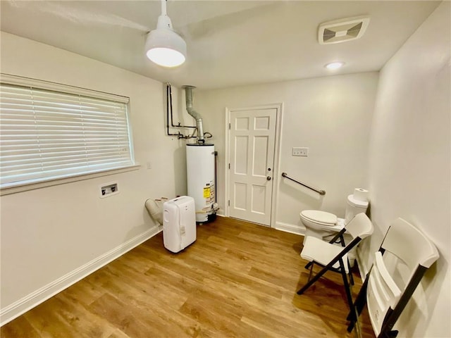 interior space with wood finished floors, visible vents, water heater, and baseboards