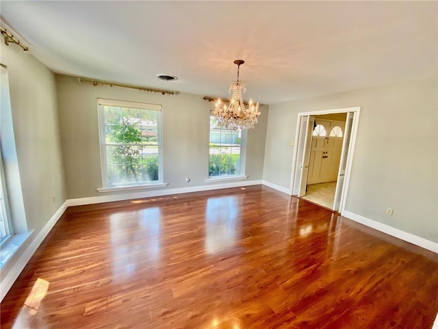 unfurnished room featuring visible vents, a notable chandelier, wood finished floors, and baseboards