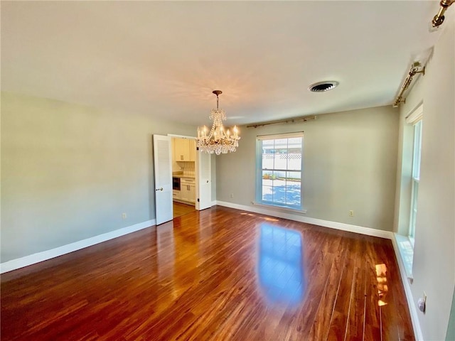 spare room with a notable chandelier, baseboards, dark wood-type flooring, and visible vents