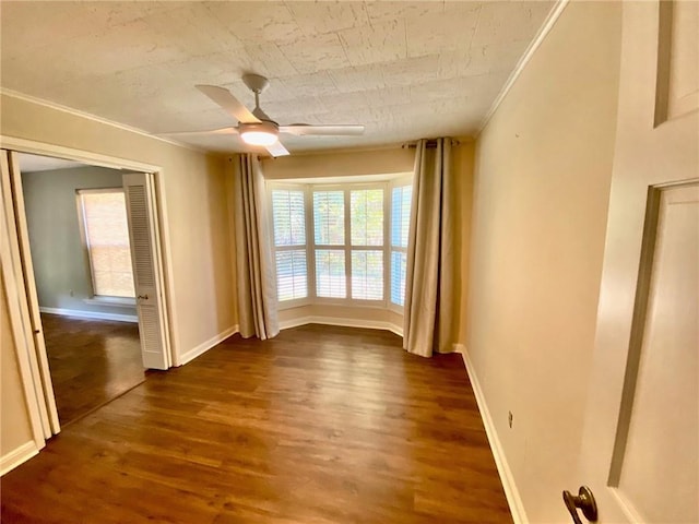 spare room featuring baseboards, dark wood finished floors, a ceiling fan, and ornamental molding