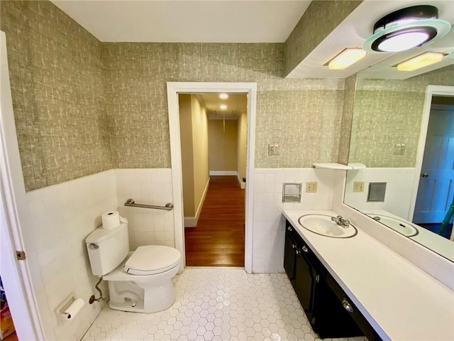 bathroom with vanity, wallpapered walls, wainscoting, tile walls, and toilet