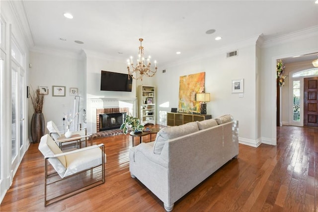 living room featuring a chandelier, hardwood / wood-style flooring, a brick fireplace, and ornamental molding