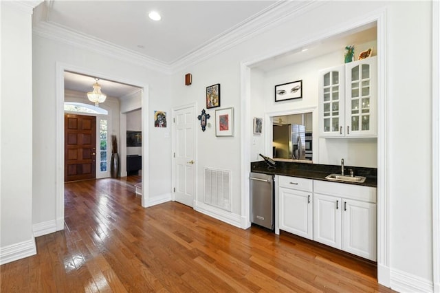 interior space featuring appliances with stainless steel finishes, crown molding, sink, wood-type flooring, and white cabinetry