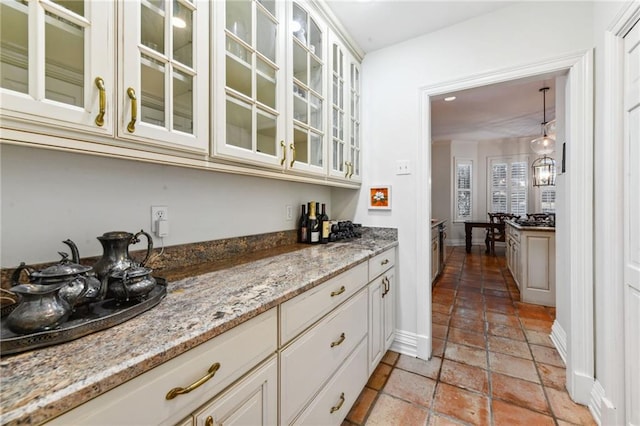 bar with light stone countertops, white cabinetry, and hanging light fixtures