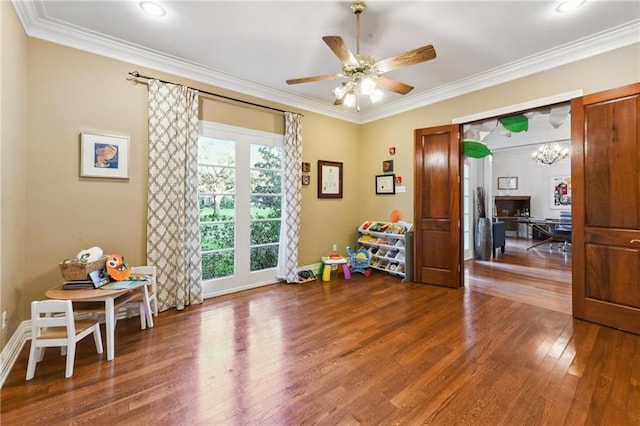 game room with wood-type flooring, ceiling fan with notable chandelier, and ornamental molding