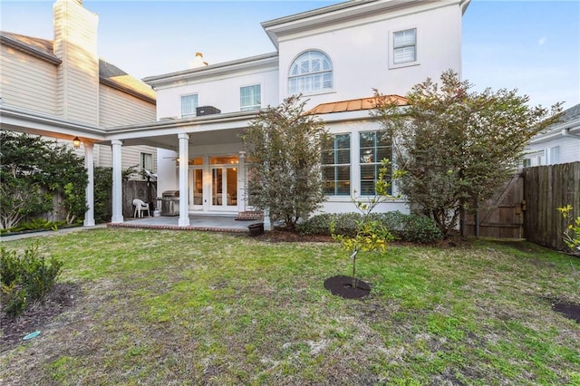 rear view of property featuring a lawn, a patio, and french doors