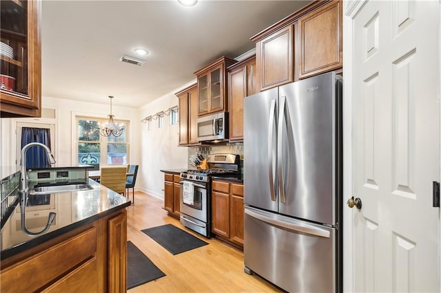 kitchen with pendant lighting, sink, appliances with stainless steel finishes, a notable chandelier, and light hardwood / wood-style floors