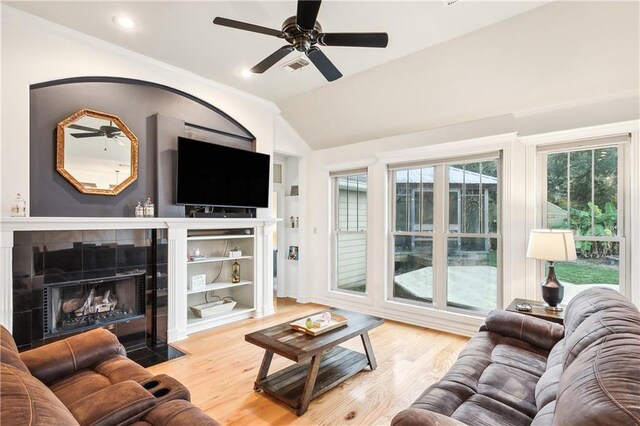 living room featuring hardwood / wood-style flooring, ceiling fan, lofted ceiling, and a tiled fireplace