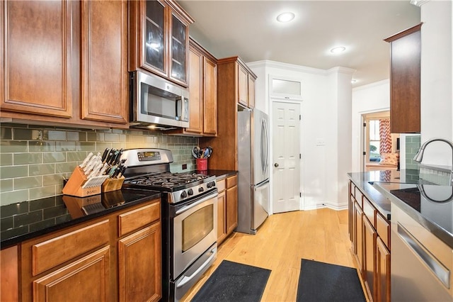 kitchen featuring appliances with stainless steel finishes, tasteful backsplash, ornamental molding, sink, and light hardwood / wood-style flooring