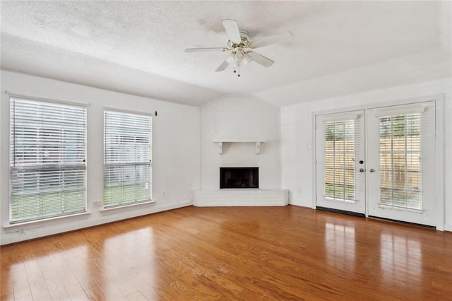 unfurnished living room with a textured ceiling, ceiling fan, a fireplace, hardwood / wood-style floors, and lofted ceiling