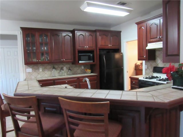 kitchen with a breakfast bar area, tile countertops, kitchen peninsula, and black appliances