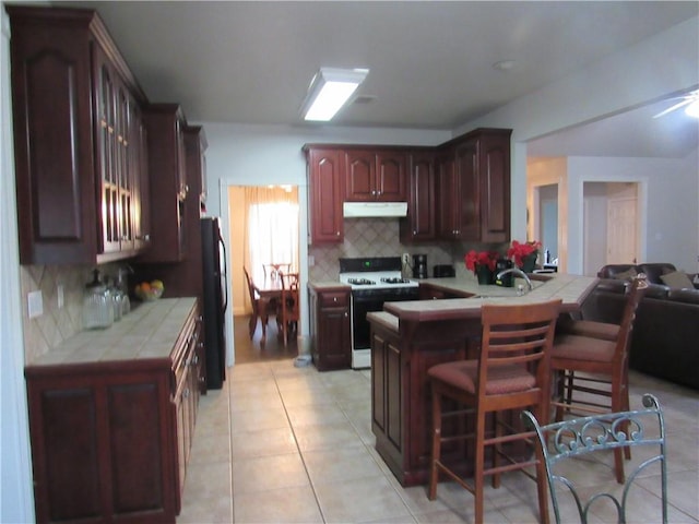 kitchen with white stove, black fridge, decorative backsplash, tile counters, and kitchen peninsula