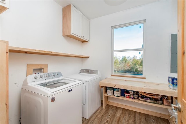 clothes washing area with cabinets, electric panel, light hardwood / wood-style flooring, and washing machine and clothes dryer