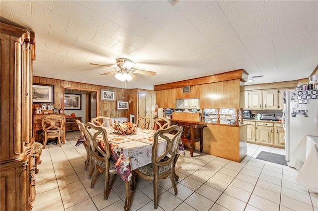 dining space with ceiling fan, wooden walls, and light tile patterned floors