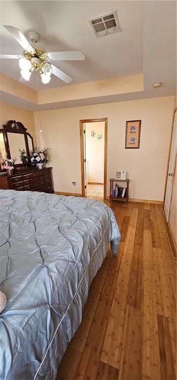 bedroom featuring wood-type flooring, a raised ceiling, and ceiling fan