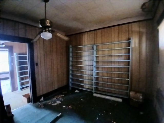 interior space featuring ceiling fan and wooden walls