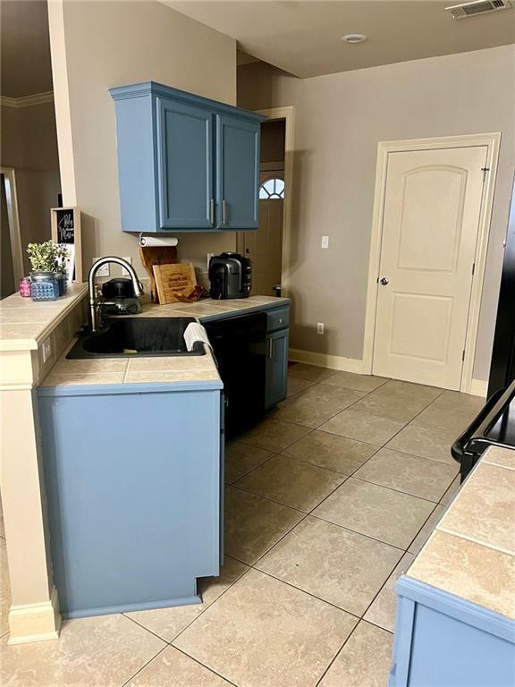 kitchen featuring blue cabinetry, light tile patterned floors, light countertops, and a sink