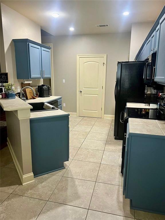 kitchen with light tile patterned floors, light countertops, visible vents, a sink, and a peninsula