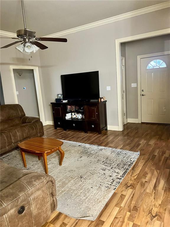 living room with ceiling fan, ornamental molding, wood finished floors, and baseboards