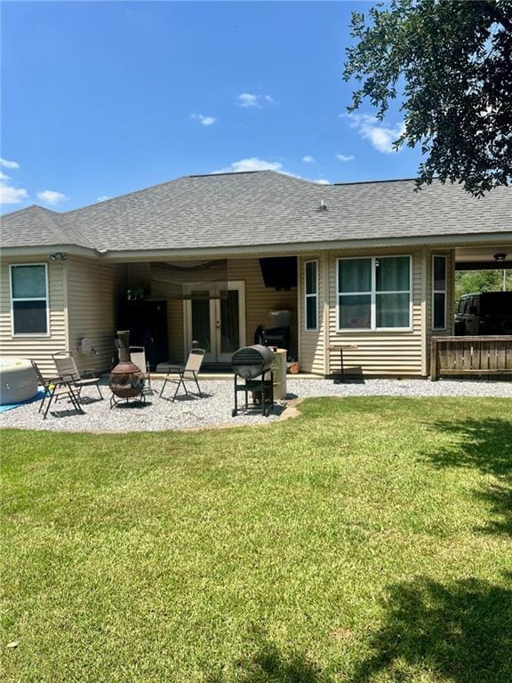 rear view of house with a patio, a fire pit, a shingled roof, french doors, and a lawn