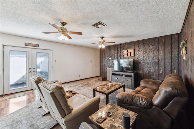 living room featuring wood walls, light hardwood / wood-style floors, a textured ceiling, and french doors