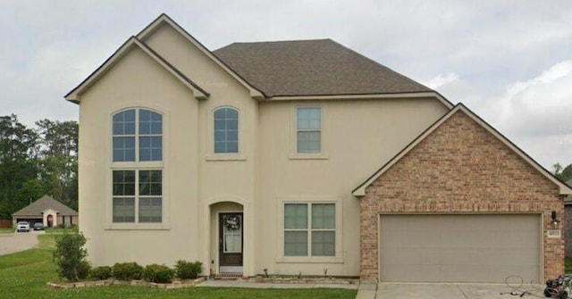 view of front of house featuring an attached garage, brick siding, a shingled roof, driveway, and stucco siding