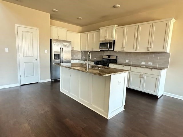 kitchen with stainless steel appliances, dark stone countertops, a sink, and white cabinetry