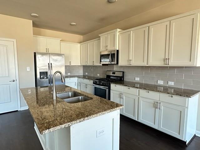 kitchen featuring tasteful backsplash, dark stone counters, appliances with stainless steel finishes, white cabinetry, and a sink