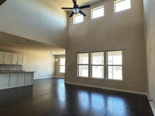 unfurnished living room with baseboards, dark wood finished floors, a towering ceiling, a sink, and ceiling fan with notable chandelier