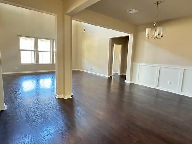 spare room featuring a chandelier, dark wood finished floors, visible vents, and a decorative wall