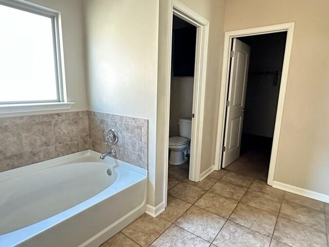 full bathroom featuring toilet, a garden tub, tile patterned flooring, and baseboards