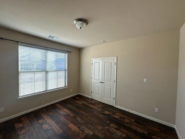 unfurnished room with dark wood-type flooring, visible vents, and baseboards