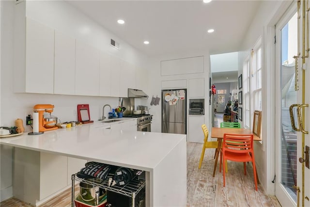 kitchen featuring white cabinets, light hardwood / wood-style floors, kitchen peninsula, and stainless steel appliances