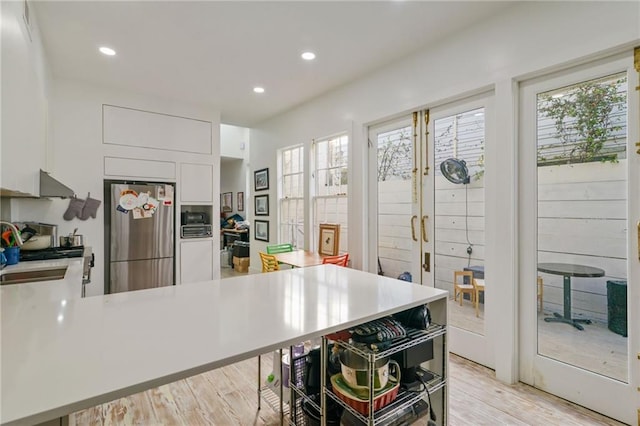 kitchen with white cabinets, a healthy amount of sunlight, light wood-type flooring, and stainless steel refrigerator