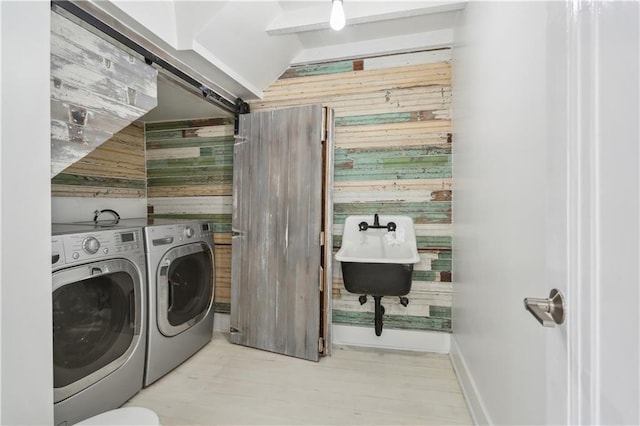 laundry area with washer and dryer, a barn door, wooden walls, and sink