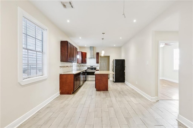 kitchen featuring appliances with stainless steel finishes, wall chimney exhaust hood, ceiling fan, pendant lighting, and a kitchen island