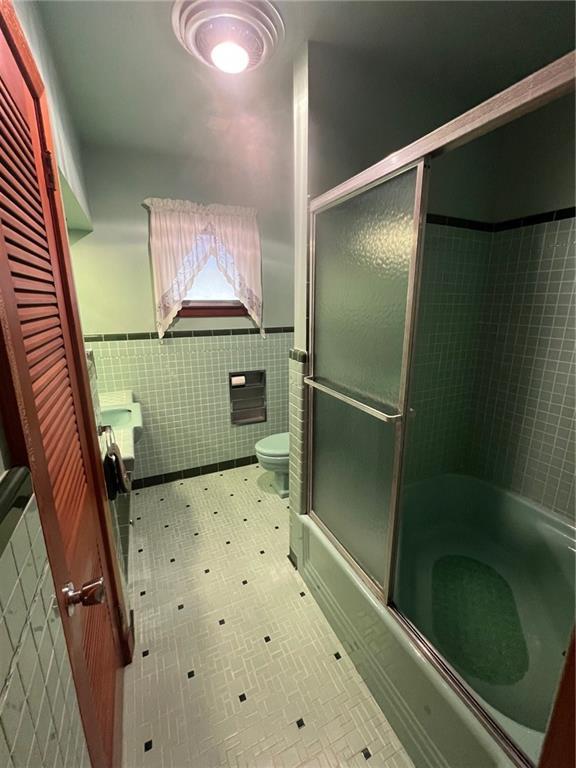 bathroom with shower / bath combination with glass door, tile walls, and toilet