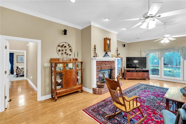 living room featuring ceiling fan, a fireplace, light hardwood / wood-style floors, and ornamental molding